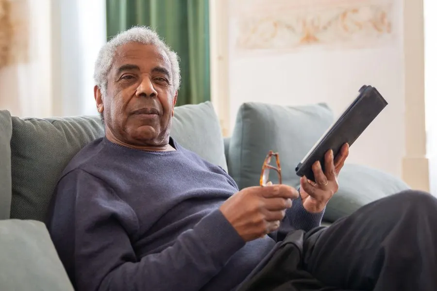 An older man relaxes on the couch with his tablet.