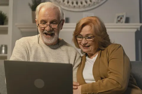An older couple smiles during a video call on a laptop.